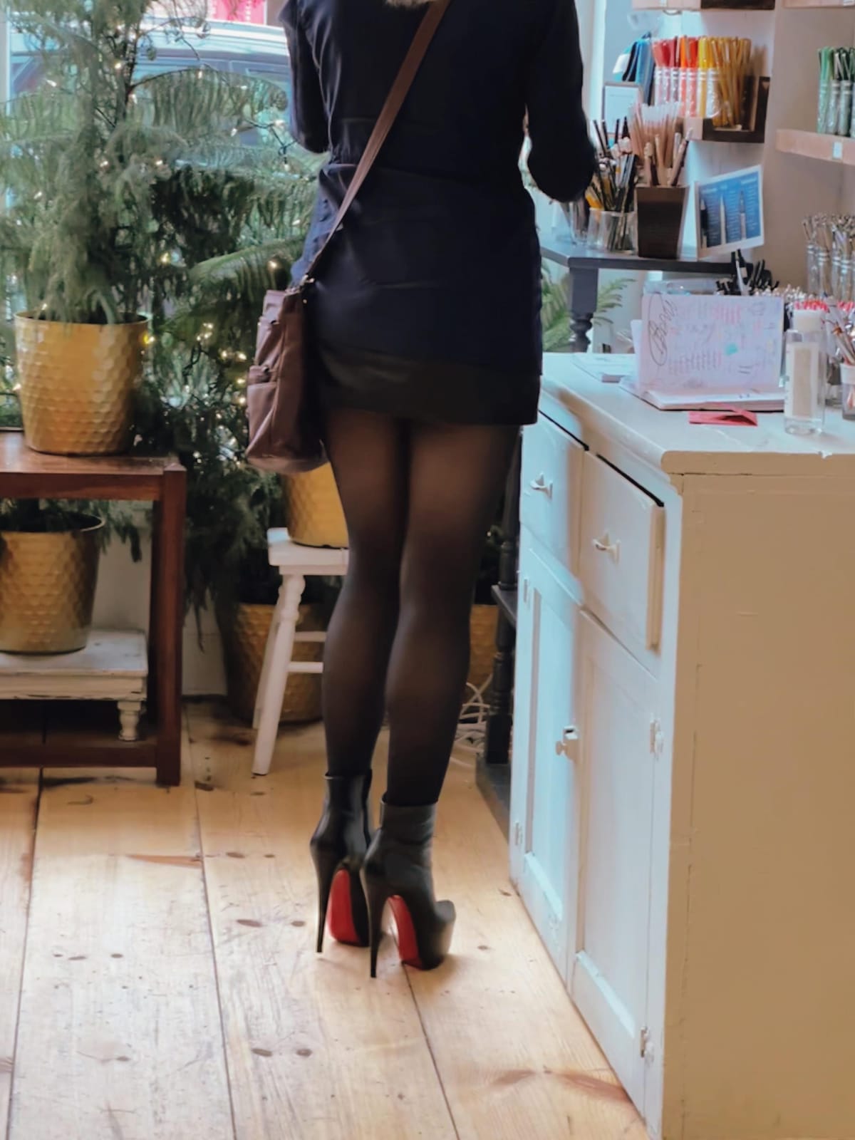 Red-soled heels with a navy coat and leather mini in a shop